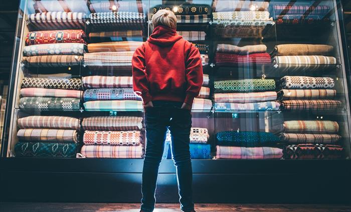 a boy in a red hoodie and jeans stands with his back to us. He is looking at a huge glass display case than goes from the floor to the ceiling. the ca